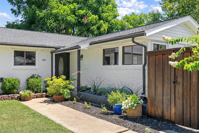 view of front facade with brick siding, a shingled roof, and fence