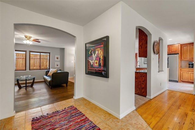 hallway featuring arched walkways, light wood-style flooring, and baseboards