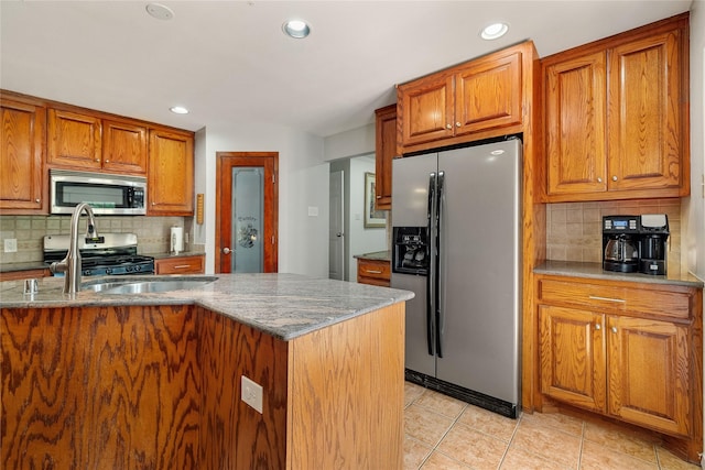 kitchen with stone counters, light tile patterned floors, stainless steel appliances, decorative backsplash, and brown cabinetry