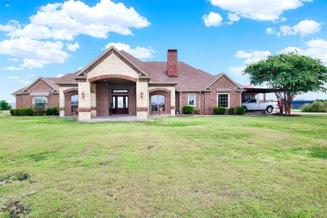 french country home with brick siding, a chimney, a shingled roof, a front yard, and a carport