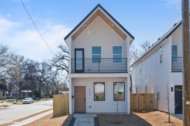 modern home with a balcony, fence, and stucco siding