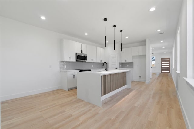 kitchen with a kitchen island with sink, a sink, white cabinets, decorative backsplash, and stainless steel microwave