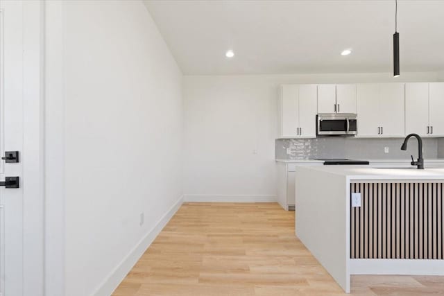 kitchen with tasteful backsplash, light countertops, stainless steel microwave, light wood-style flooring, and a sink