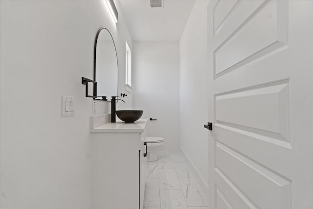 half bathroom featuring visible vents, baseboards, toilet, marble finish floor, and vanity