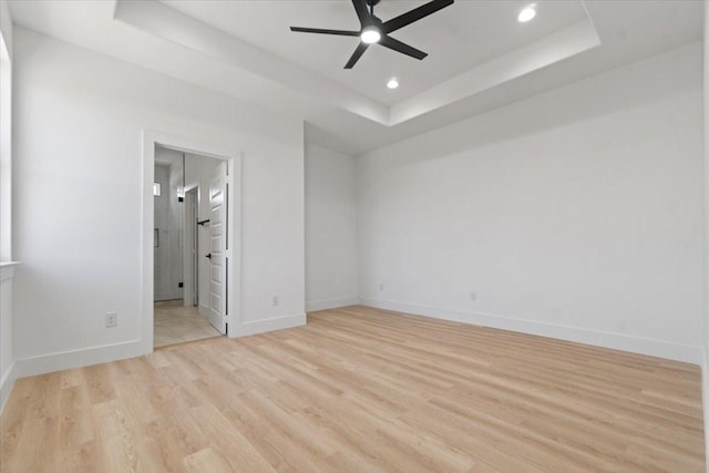 unfurnished bedroom featuring baseboards, a raised ceiling, ensuite bath, light wood-style floors, and recessed lighting