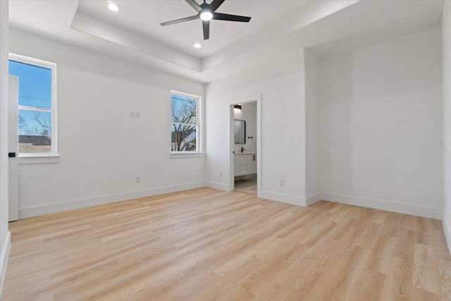 unfurnished bedroom with light wood finished floors, multiple windows, baseboards, and a raised ceiling