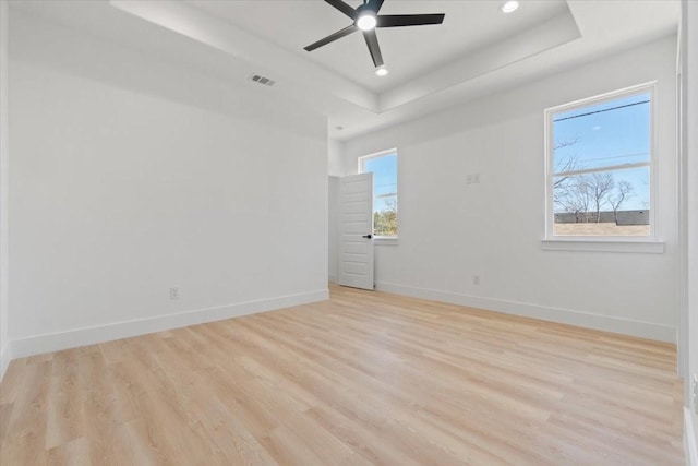 empty room with a tray ceiling, light wood-type flooring, visible vents, and baseboards