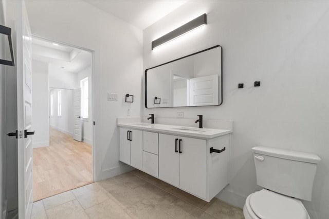 bathroom with baseboards, a sink, toilet, and double vanity