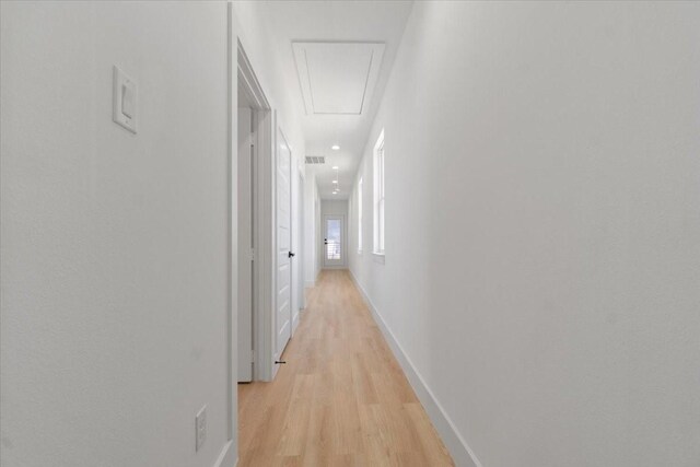 hallway with light wood-type flooring, attic access, visible vents, and baseboards