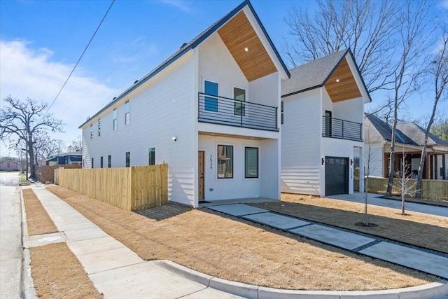 view of front of house featuring driveway, fence, a balcony, and stucco siding