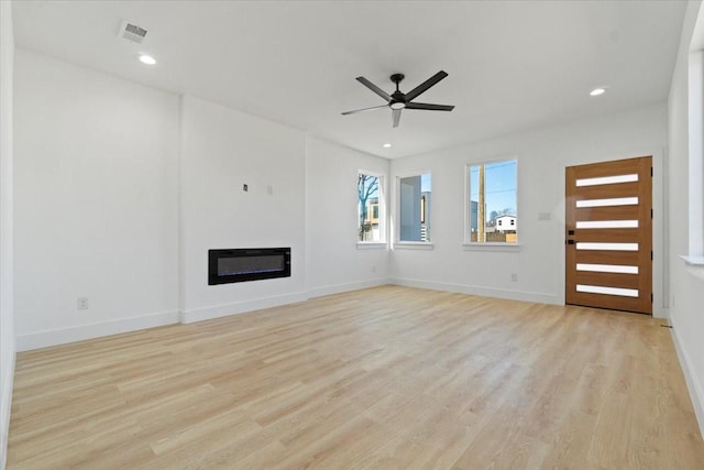 unfurnished living room with heating unit, visible vents, light wood-style floors, a glass covered fireplace, and a ceiling fan