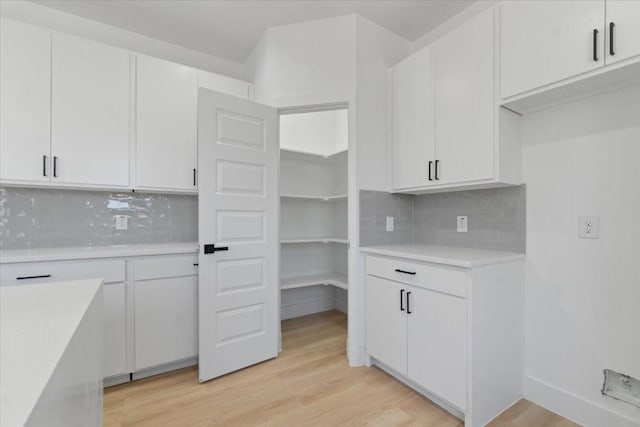 kitchen with white cabinets, light countertops, light wood-style flooring, and backsplash