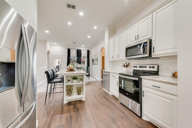 kitchen featuring light wood finished floors, arched walkways, appliances with stainless steel finishes, white cabinetry, and backsplash