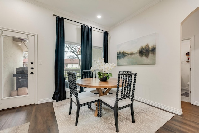 dining area featuring ornamental molding, arched walkways, dark wood-style flooring, and baseboards