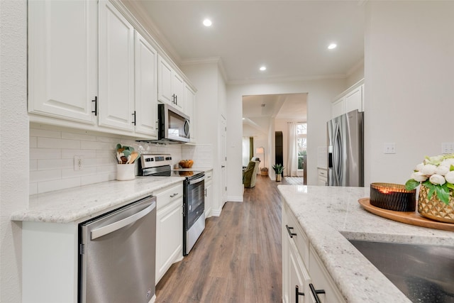 kitchen with tasteful backsplash, appliances with stainless steel finishes, white cabinets, and crown molding