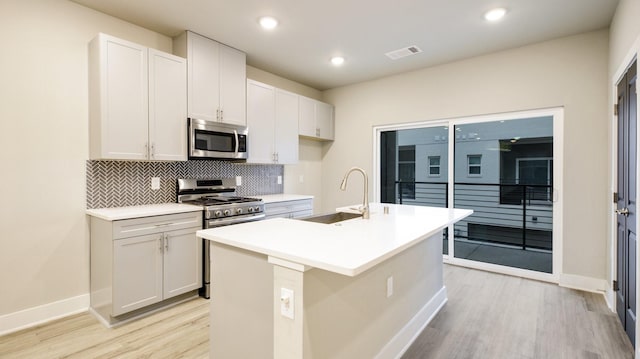 kitchen with visible vents, backsplash, appliances with stainless steel finishes, a kitchen island with sink, and a sink