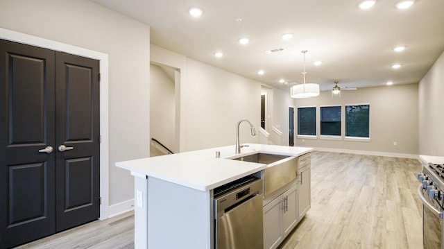 kitchen featuring stainless steel appliances, visible vents, light wood-style floors, a sink, and an island with sink