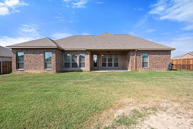 rear view of property with brick siding, a patio, a shingled roof, a lawn, and fence private yard