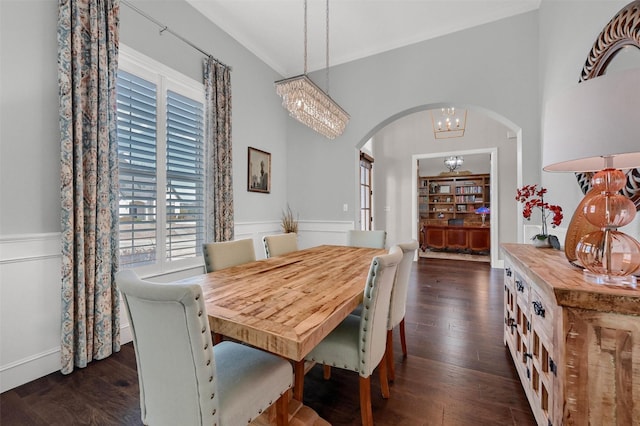 dining space with dark wood-style floors, a wainscoted wall, arched walkways, crown molding, and a notable chandelier