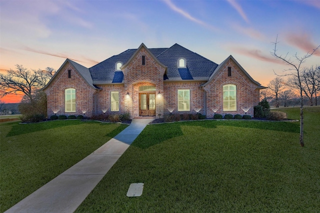 french country style house featuring brick siding, a front yard, and roof with shingles