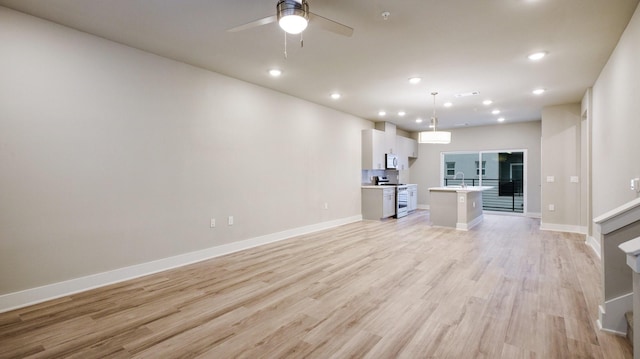 unfurnished living room featuring light wood finished floors, baseboards, a ceiling fan, a sink, and recessed lighting