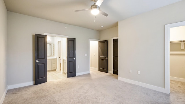 unfurnished bedroom with baseboards, ensuite bath, a walk in closet, and light colored carpet