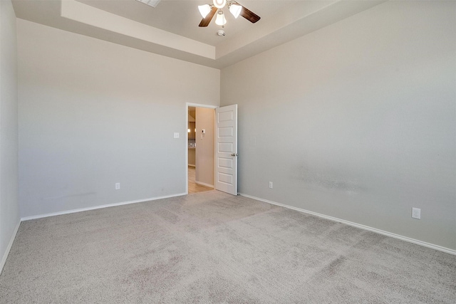 carpeted spare room featuring a ceiling fan, a tray ceiling, a high ceiling, and baseboards