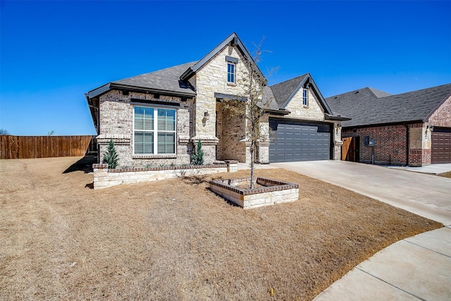 french country home featuring an attached garage, fence, driveway, stone siding, and roof with shingles