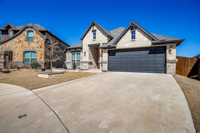 french country home with an attached garage, stone siding, fence, and concrete driveway