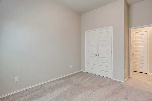 unfurnished bedroom with a closet, light colored carpet, and baseboards