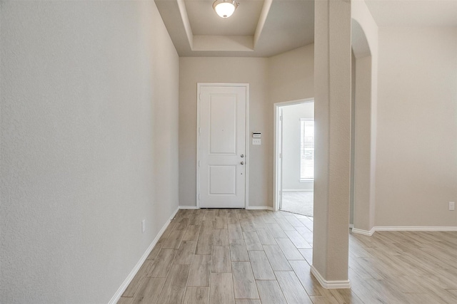 entryway featuring light wood-type flooring, a tray ceiling, arched walkways, and baseboards