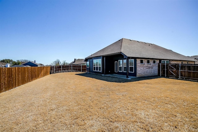 back of house featuring a yard, brick siding, a patio area, and a fenced backyard