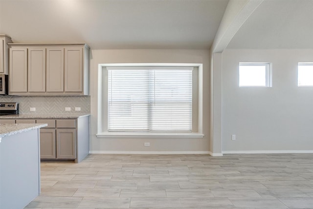 kitchen with tasteful backsplash, baseboards, appliances with stainless steel finishes, light stone counters, and gray cabinetry