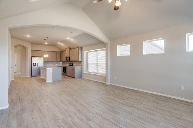 kitchen featuring a kitchen island with sink, open floor plan, light countertops, appliances with stainless steel finishes, and decorative backsplash