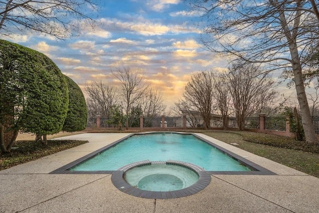 pool at dusk with a pool with connected hot tub, fence, and a patio