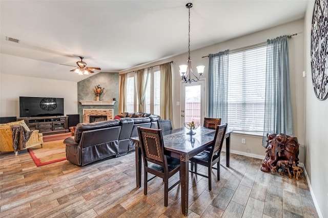 dining area featuring ceiling fan with notable chandelier, a fireplace, wood finished floors, and visible vents