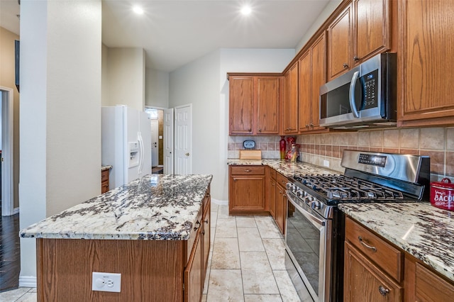 kitchen with brown cabinets, decorative backsplash, light stone counters, and stainless steel appliances