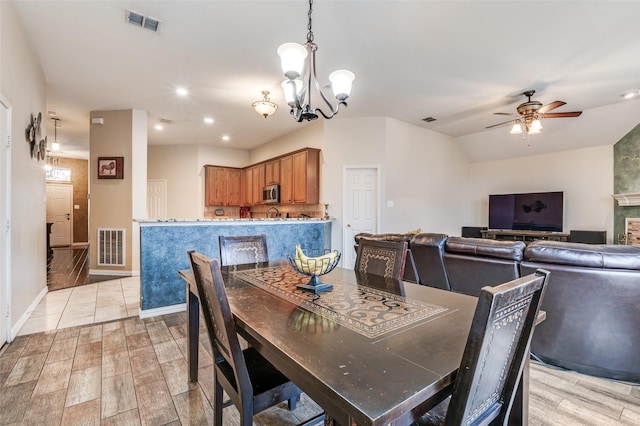 dining space with lofted ceiling, visible vents, light wood-style flooring, and ceiling fan with notable chandelier