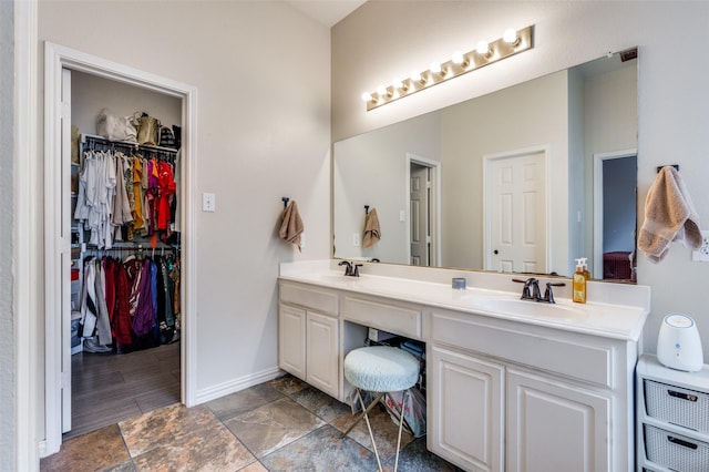 bathroom with a spacious closet, double vanity, baseboards, and a sink