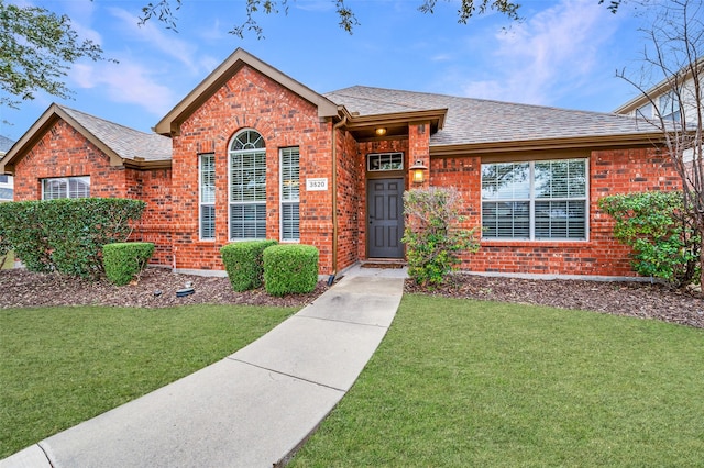 ranch-style house with a front yard, brick siding, and roof with shingles