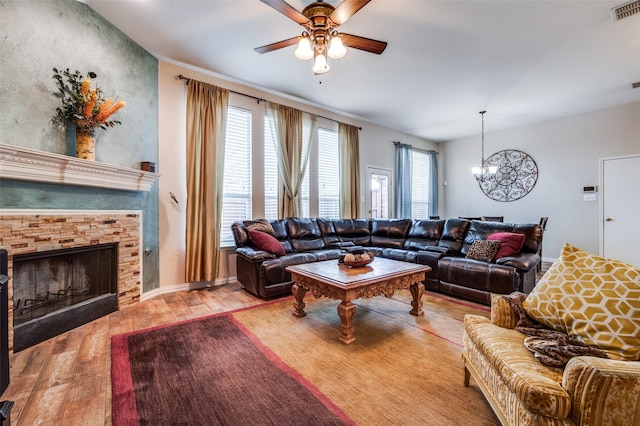 living room with wood finished floors, ceiling fan with notable chandelier, a fireplace, and visible vents