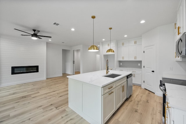 kitchen featuring a large fireplace, visible vents, stainless steel appliances, white cabinetry, and a sink