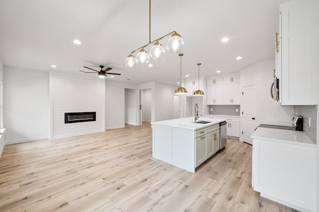 kitchen featuring stainless steel dishwasher, light wood-style floors, a large fireplace, a kitchen island with sink, and a sink