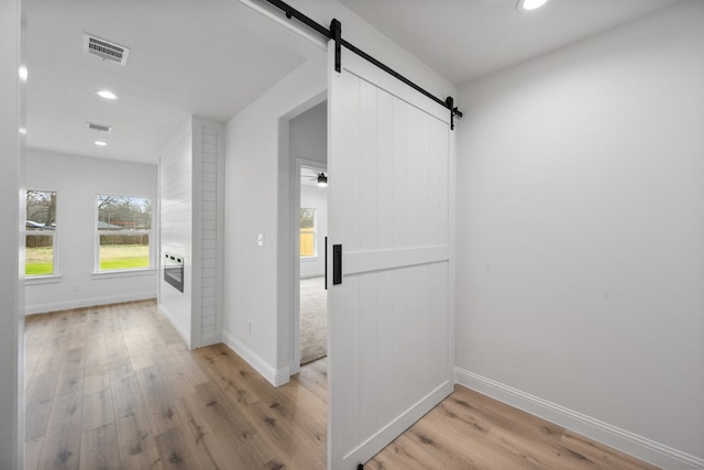 hall with baseboards, a barn door, visible vents, and wood finished floors