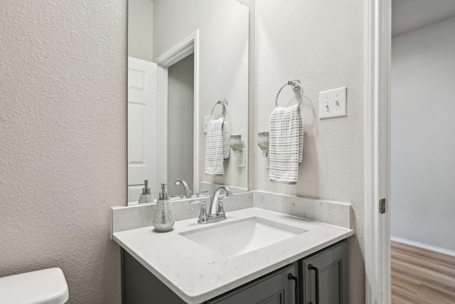 bathroom with toilet, a textured wall, wood finished floors, and vanity