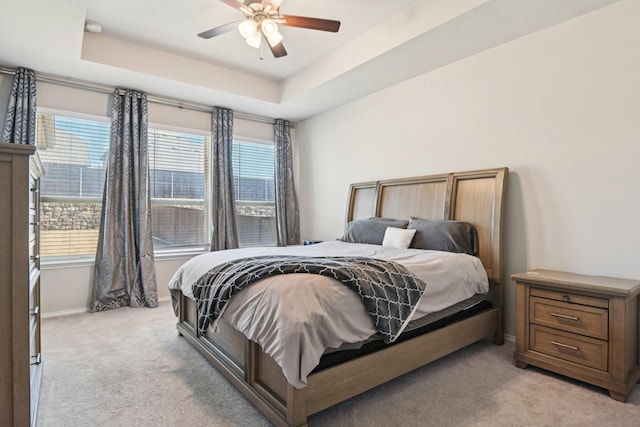 bedroom with a tray ceiling, multiple windows, and light colored carpet