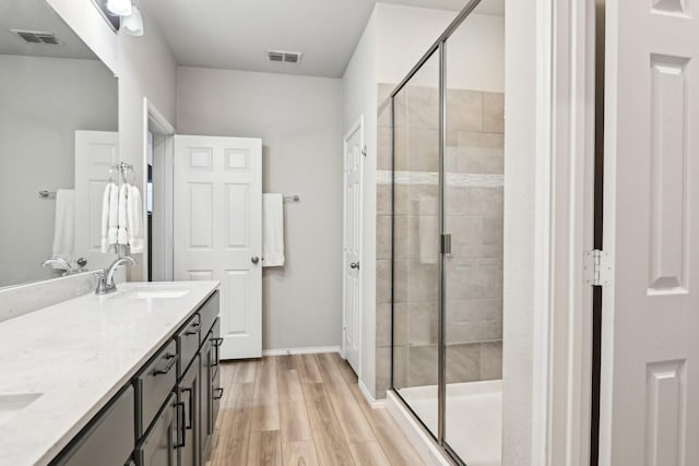 bathroom with wood finished floors, a sink, visible vents, a shower stall, and double vanity