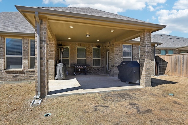 rear view of house with brick siding, a patio area, fence, and a shingled roof