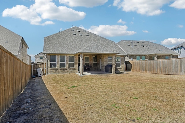 rear view of property featuring a fenced backyard, brick siding, a yard, roof with shingles, and a patio area