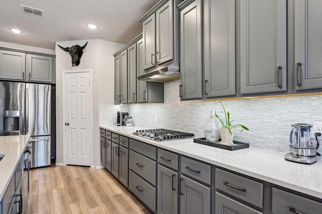 9017 Cattle Herd Dr, Fort Worth, TX 76123 - kitchen with stainless steel appliances, under cabinet range hood, gray cabinets, light wood-type flooring, and tasteful backsplash